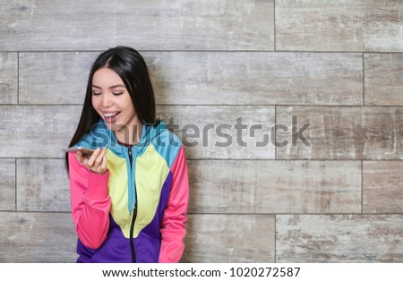 Happy young woman with mobile phone near wooden wall