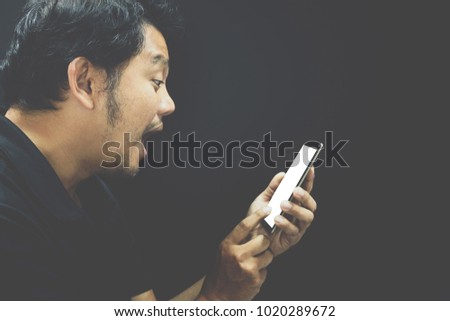Asian man 40s have a short hair with a beard in black polo shirt stunned and surprise gesture using smartphone on black background dark style