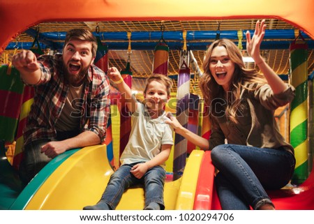 Cheerful little boy sitting on a slidewith his parents at Arcade centre