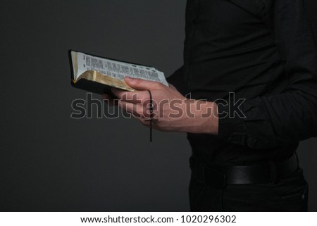 The hands of the priest preserve an open bible with a cross