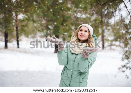 Young beautiful slender blonde girl outdoors in winter is catching her hands walking snow and snowflakes and smiling. Portrait of an attractive model on a winter background. 