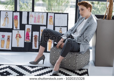 beautiful fashion designer sitting at office in front of board with various sketches