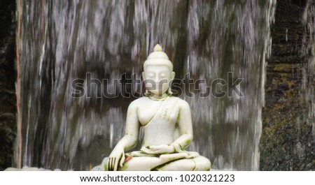 White buddha statue or buddha image made of marble. Plate on the rocks with a waterfall background in temple of Thailand. The Buddhist It will pay homage to the statue of the Buddha is represented.