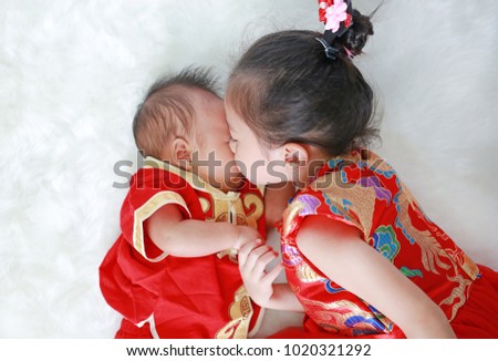 Adorable little asian girl kissing infant baby boy in cheongsam lying on white fur background during traditional chinese new year festival.