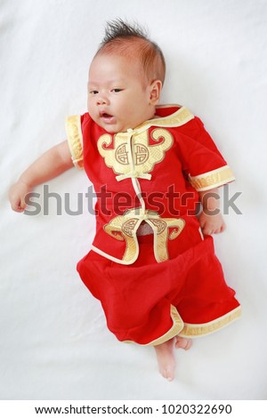 Infant baby boy in cheongsam lying on white fur background during traditional chinese new year festival.