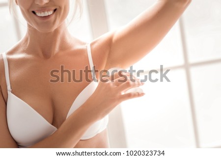 Always fresh. Happy positive joyful woman smiling and holding her arm up while using deodorant