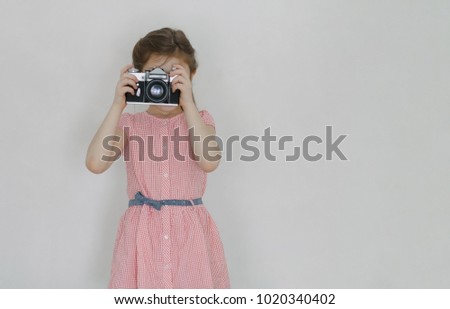 Fashion pretty young smiling girl holds retro camera wearing red dress, over white background