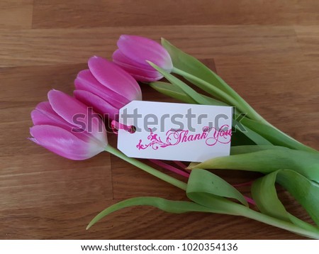 Tulips with a thank you note laying on a wooden table