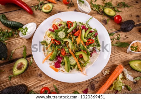 Tortilla with avocados and vegetables on wooden background
