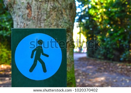 The square wooden walk sign on the bottom left and in front of brown trunk with background blurred pathway and green trees, feeling safe, free space for texts. Concept Walking symbol.
