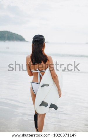 back view of girl in bikini holding surfboard on beach