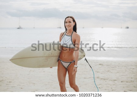 attractive surfer in swimsuit walking with surfboard on beach at sea