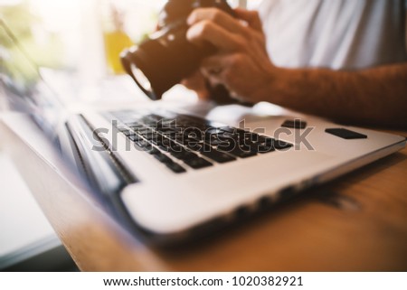 Very close shot of laptop and professional camera in male hands working with it-