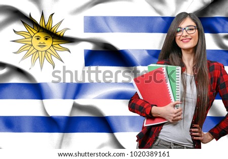 Happy female student holdimg books against national flag of Uruguay