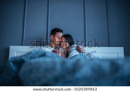 Young couple lying in bed at night , holding a mobile phone