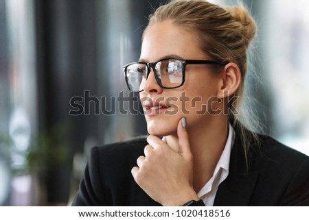 Picture of young serious business woman sitting indoors in cafe looking aside.