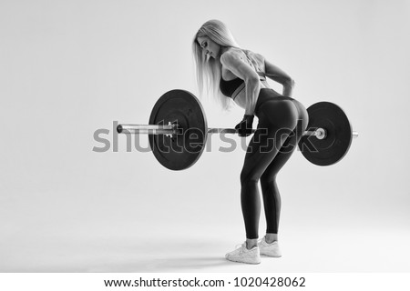 Black and white photo of confident young woman doing weight lifting workout at gym turning back Attractive young woman bodybuilder lifting barbells looking focused