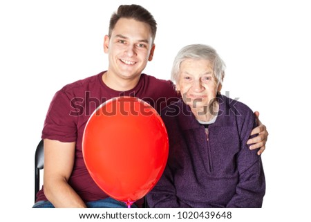 Picture of a smiling grandmother and her cheerful grandson embracing and holding a red balloon