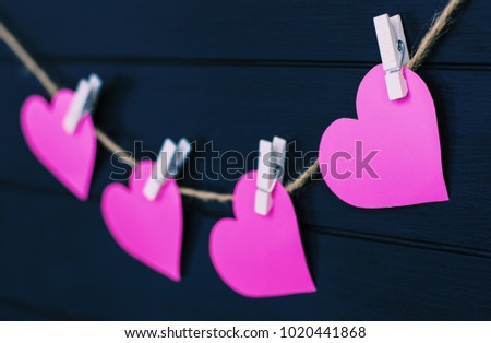 Pink paper hearts hanging on rope on dark wooden background. Valentine's background.