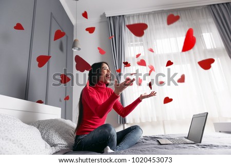 Beautiful, happy, young woman throwing red heart-shapes in the air, sitting on the bed Royalty-Free Stock Photo #1020453073