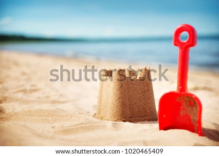 Sandcastle with a shovel on the sea in summertime. Seashore on beautiful day. Sand on the beach and blue water Royalty-Free Stock Photo #1020465409