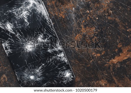 Modern smartphone with large broken screen with debris on the grunge backgdound with copy space