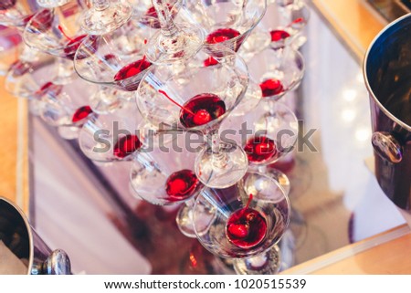 Glasses for champagne with a cherry inside on the table, ready to celebrate. Slide champagne on the mirror table. Closeup. Stylishly toned photo