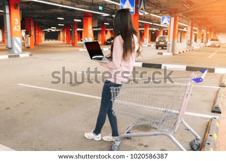 Traveler woman using laptop on car parking reading guide book map on pc, using mobile internet, relaxing by the auto with car parking in background