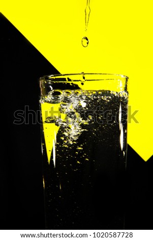 Water is poured into a transparent glass on a bright yellow and black background. Bubbles in the water