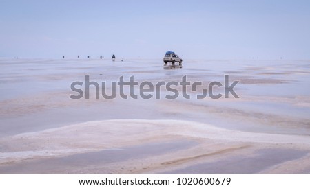 Photo of an SUV car driving through the middle of the endless flat blue emptiness covered by water producing nice patterns in the ground. Captured at Uyuni Salt Flats, Bolivia. Infinity feeling. 