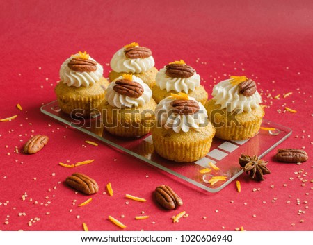 Cupcakes decorated with pecan nuts, orange zest and spice on red background