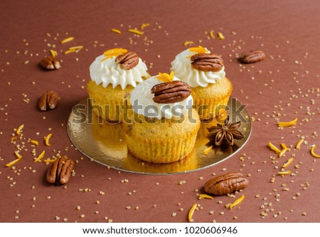 Cupcakes decorated with pecan nuts, orange zest and spice on brown background