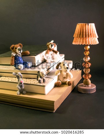 Miniature cute knitted toys sitting on books under a miniature floor lamp. Knitted toy: teddy bears, dogs, bunny on black background. Club of book lovers. Picture for children's wallpapers, postcards.