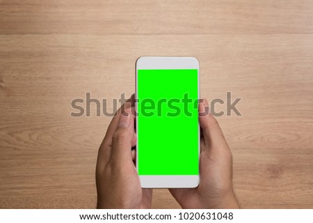 Man hand holding the smartphone with green screen isolated on wooden background.
