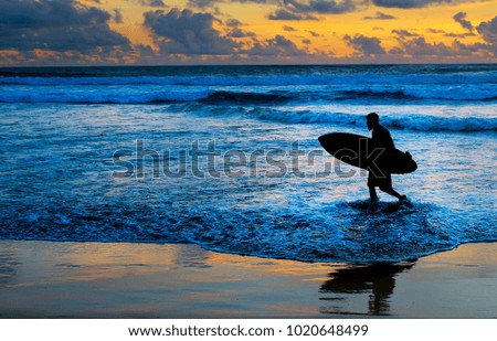 Surfer on the beach with surfboard at sunset. Bali island