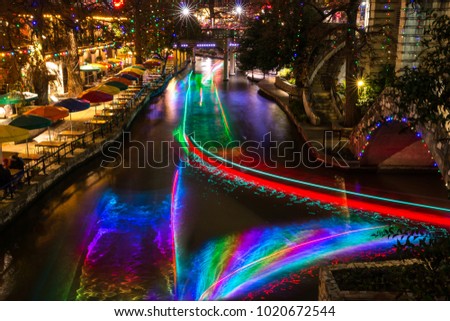 San Antonio Riverwalk at night Christmas time with some skyline.  Long exposure streaks colored light through the water from tour barges.
