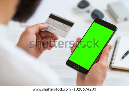 A black smartphone with green screen for chroma key compositing and a credit card in the hands of a man on a rural white background, concepts of Internet commerce and the use of online banking to pay 