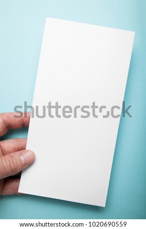 Hand holding vertical blank flyer brochure booklet on blue background. Leaflet presentation.