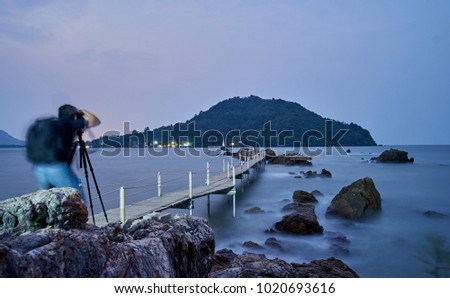 wooden bridge to the sea bay nearly the rock with green mountain background and moving photographer he capturing the same view.