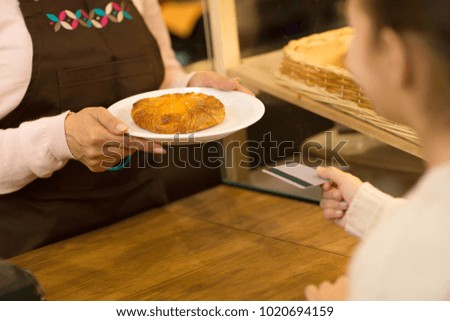 Cropped shot of a female professional baker giving a plate with pastry to a little girl paying with her credit card buying food at the cafe bakery store consumerism payment money banking.