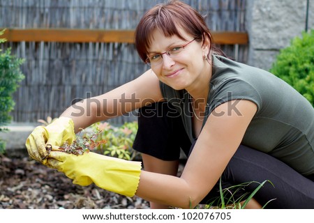 smiling middle age woman gardener with flowers outdoor in her garden Royalty-Free Stock Photo #102076705