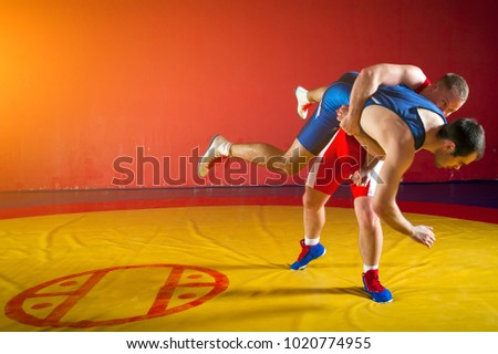 Two greco-roman  wrestlers in red and blue uniform wrestling  on background on a yellow wrestling carpet in the gym