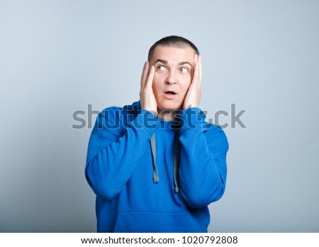 portrait of a man frightened, wearing a blue hoodie, isolated on a gray background