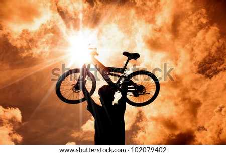 The Silhouette of mountain biker raised bicycle with sunset and cloud background