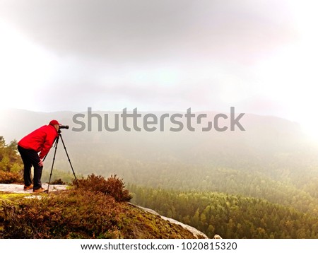 Professional photographer shooting. Artist stay  with tripod on summit and  takes pictures of autumnal coutryside. Misty landscape, cold sunrise in fall nature.