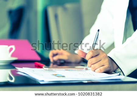 Hand of businesswoman holding with silver pen and playing a phone on documents in the office interrior
