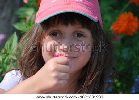 Beautiful young girl in a summer garden, wearing a baseball cap, smiling and holding a flower