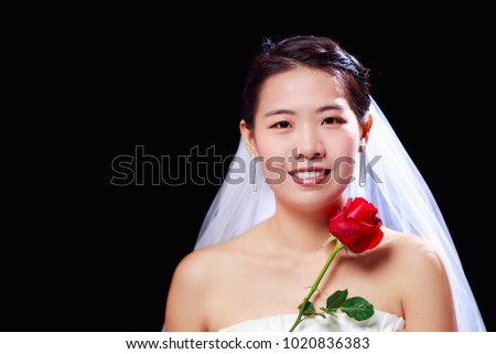 Beautiful Asian look woman in white wedding dress holding red rose flower on black background, Bride theme portrait, selected focus