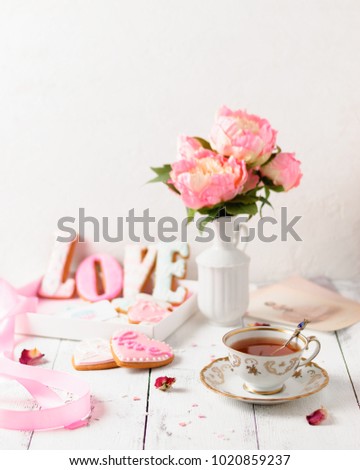 A cup of tea, pink homemade cookies with icing and bouquet of peonies to the St Valentine Day. Copy space