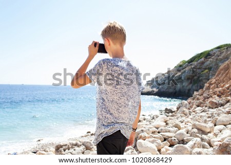 Rear of teenager young man using old photographic camera taking photos on beach landscape, practicing photo creative hobby, sunny outdoors. Male holding camera, travel leisure recreation lifestyle.